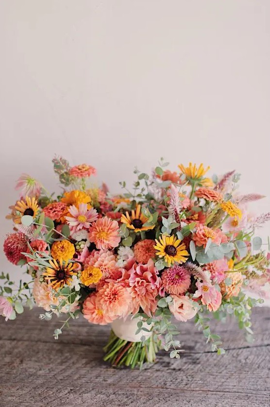 a bright summer wedding bouquet of pink and orange dahlias, some yellow and pink blooms and greenery is amazing
