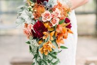 a cascading wedding bouquet of orange and burnt orange blooms, burgundy, blush flowers, thistles, greenery and pale foliage