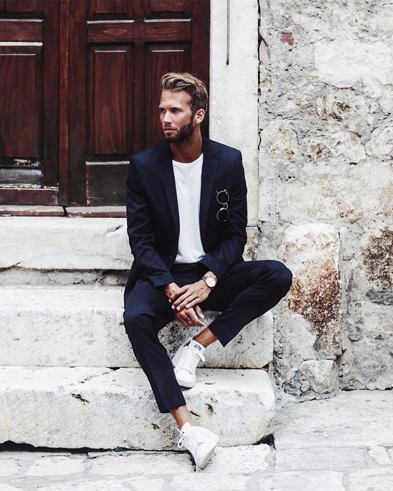 a cool laconic minimalist groom's look with a navy pantsuit, a white t-shirt and white sneakers, a watch and sunglasses