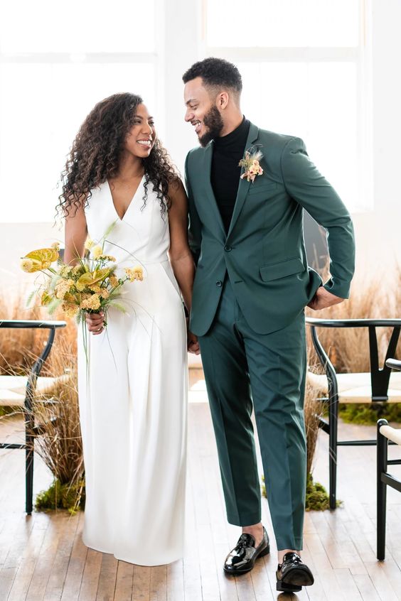 a cool modern groom's look with a grene pantsuit, a black turtleneck, black lacquer loafers and a bold floral boutonniere
