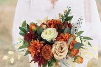 a fall wedding bouquet with burgundy and burnt orange dahlias, neutral roses, greenery and ribbon is wow