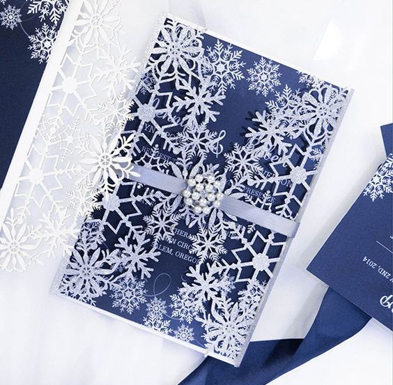 a jaw-dropping navy and silver glitter wedding invitation with snowflake print and a snaowflake jacket plus a beaded detail