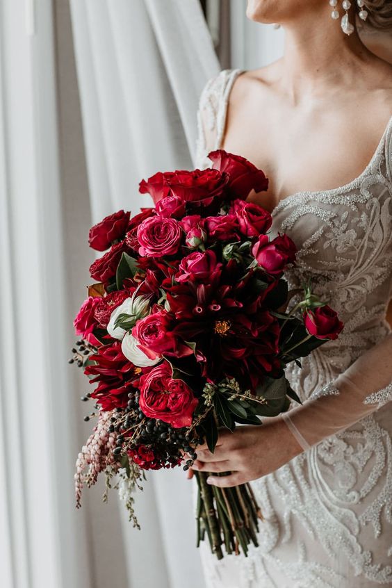 a lovely textural deep red and burgundy wedding bouquet of roses, greenery and berries is a stylish and bold idea for a colorful wedding