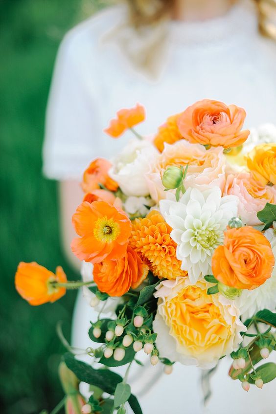 a lovely wedding bouquet of orange poppies and ranunculus, yellow, blush and white blooms and berries for summer