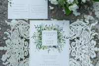 a lovely wedding invitation suite with white flower and greeneyr print and a delicate white laser cut lace invite jacket