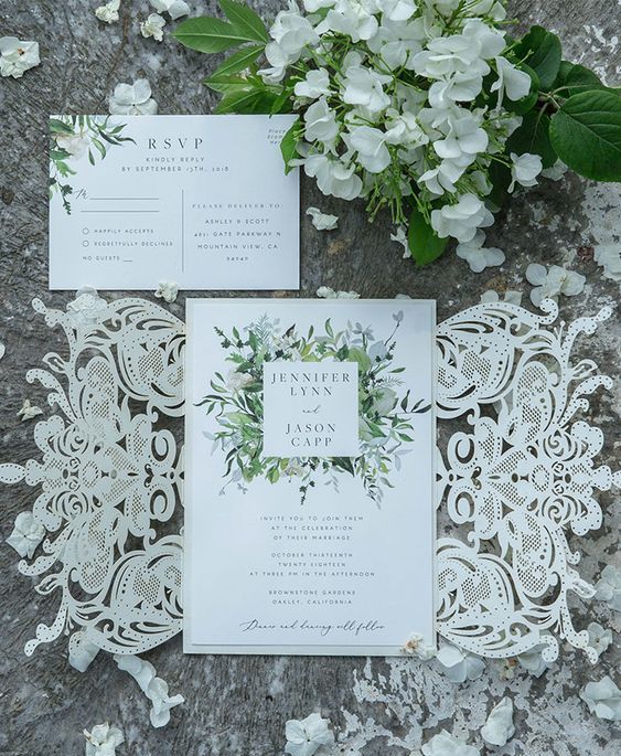 a lovely wedding invitation suite with white flower and greeneyr print and a delicate white laser cut lace invite jacket