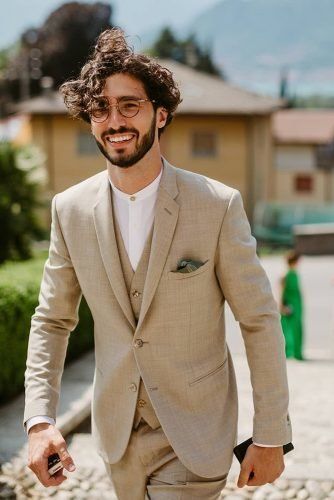 a modern and chic groom's outfit with a tan three piece suit, a white shirt, a handkerchief and round glasses