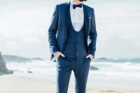 a navy three-piece suit with a white shirt, a navy bow tie and white sneakers for a relaxed feel