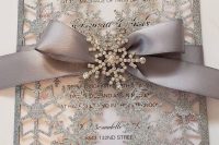 a neutral wedding invitation dressed up with a silver glitter snowflake jacket, a grey ribbon and a brooch for a winter wonderland wedding