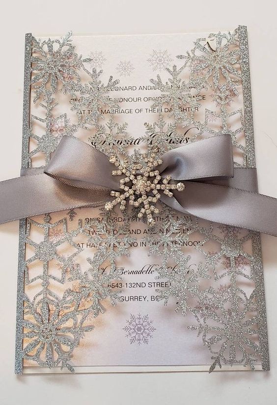 a neutral wedding invitation dressed up with a silver glitter snowflake jacket, a grey ribbon and a brooch for a winter wonderland wedding
