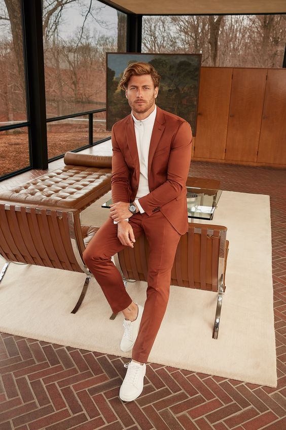 a stylish modern groom's look with a rust-colored suit, a white shirt and white sneakers is a cool idea for a fall or desert wedding