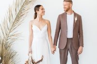 a taupe minimalist pantsuit of linen, a white t-shirt and white sneakers plus a dried flower boutonniere are a great combo for a tropical wedding