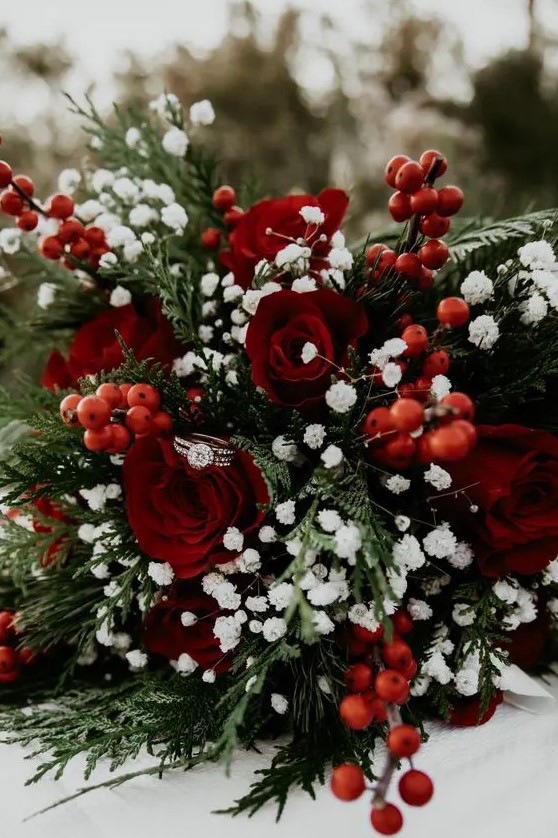 a traditional Christmas wedding bouquet of red roses, berries, greenery and baby's breath is contrasting