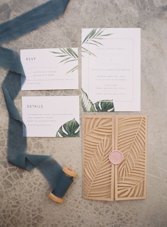 a tropical wedding invitation suite with tropical leaf prints and a laser cut leaf invitation jacket with a pink seal
