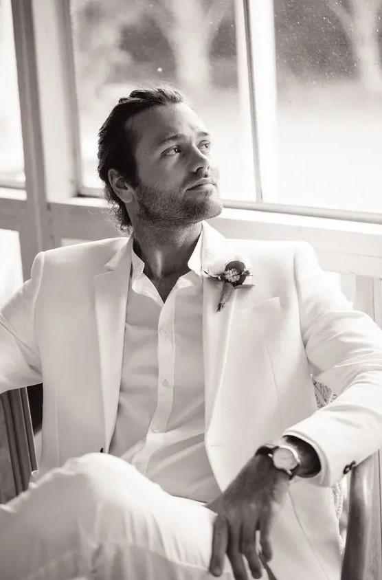 an all white look with a suit and a shirt, a bold boutonniere are a great combo for a modern tropical or summer wedding