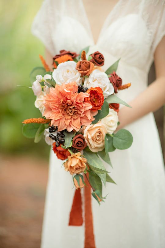 an exquisite wedding bouquet with white and orange roses, a large orange dahlias, berries and greenery with an eye-catchy shape