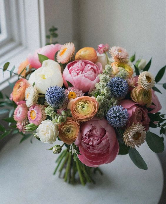a beautiful and delicate wedding bouquet with yellow ranunculus, white and pink peonies, allium and some dried blooms