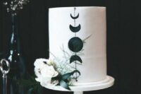 02 a white wedding cake with black moon phases and white blooms and greenery is a chic idea for a boho celestial wedding
