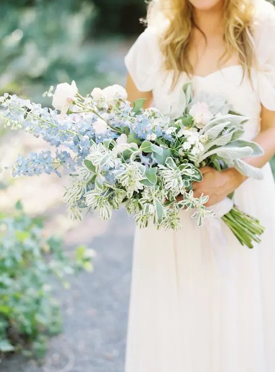 a beautiful wedding bouquet including white roses and blue delphinium and various types of greenery for a French country wedding