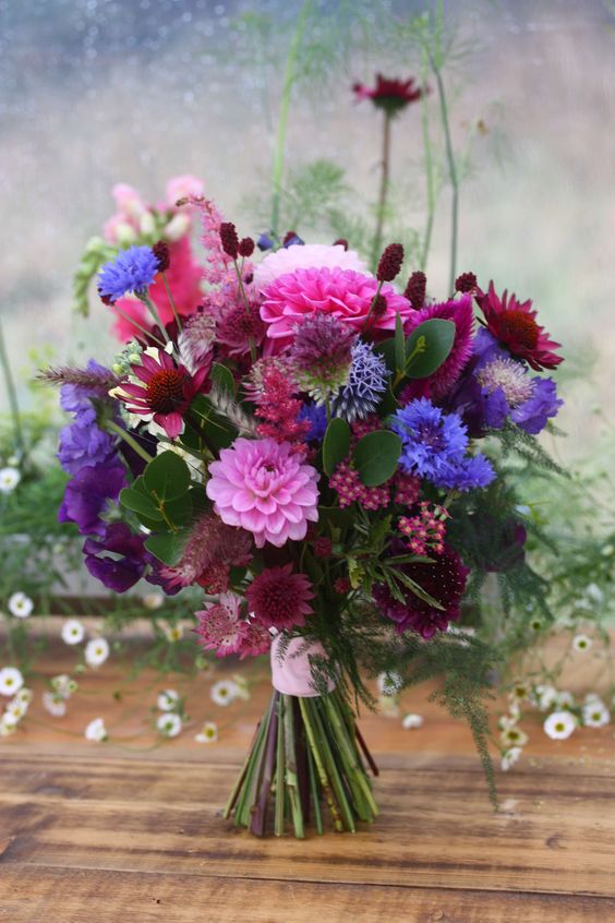 a jewel-tone wedding bouquet of pink and burgundy dahlias, bunny tails, allium and some violet blooms and foliage