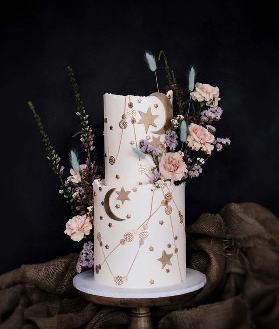 a white celestial wedding cake decorated with copper stars, polka dots, moons and dried blooms and grasses is wow