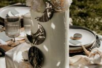a white tall wedding cake with with moon phases decorated with silver foil and topped with neutral blooms
