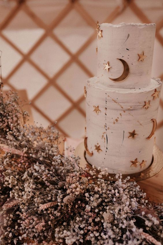 a pretty neutral wedding cake decorated with gold stars and moons and with a raw edge is a pretty idea for a celestial wedding