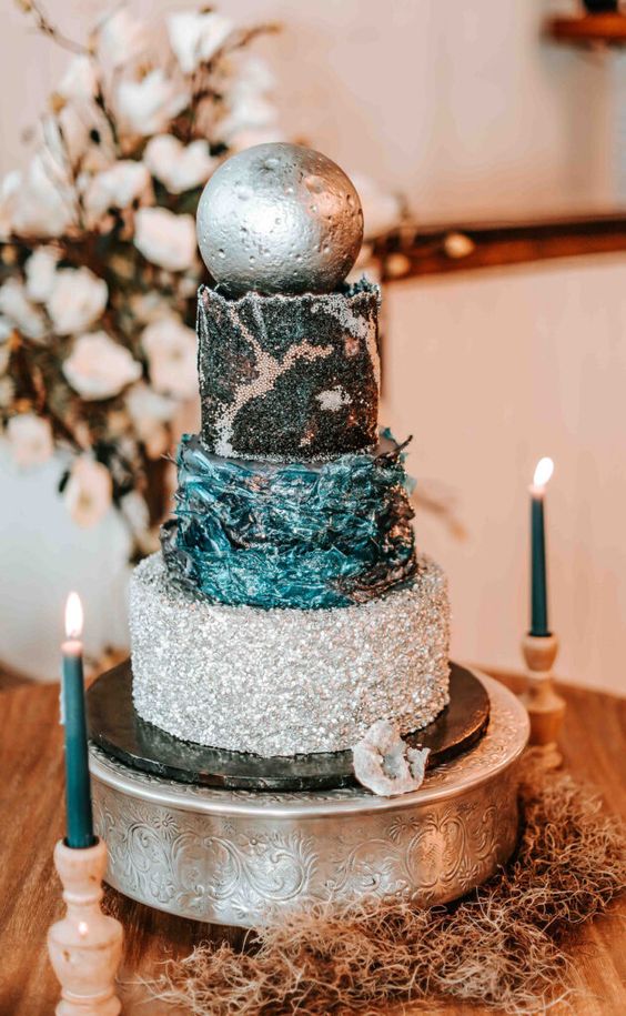 a celestial wedding cake with a silver tier, a navy textural one, a black tier with silver decor and a silver sphere on top