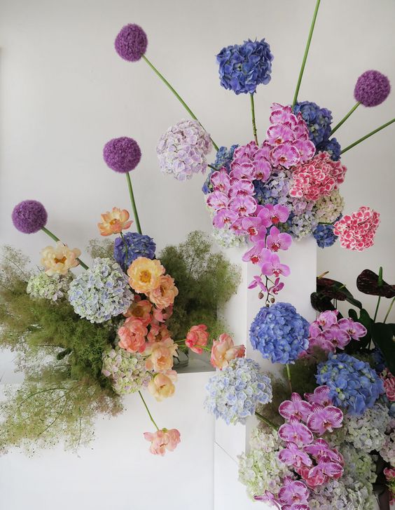 colorful modern wedding florals - pink orchids, allium, various hydrangeas and greenery in laconic square vases