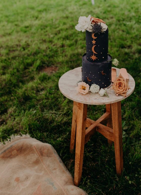 a black celestial wedding cake with silver polka dots, gold stars and half moons and white blooms and thistles on top