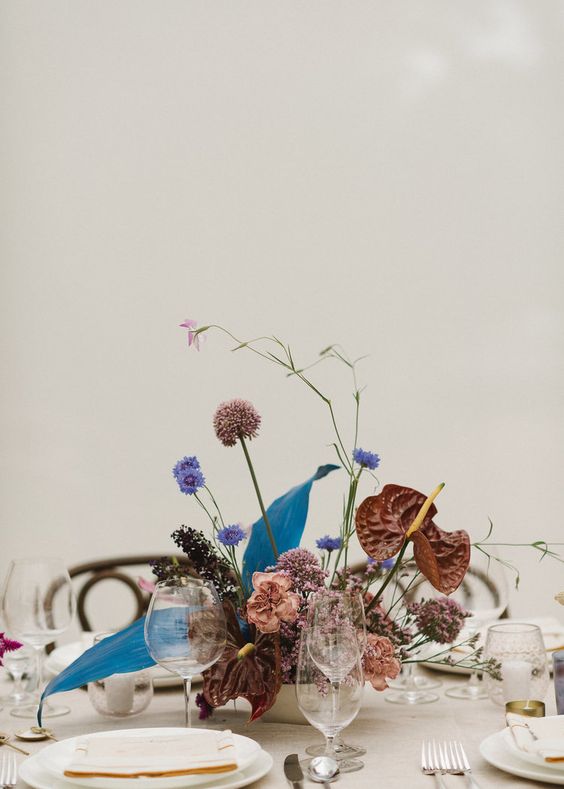 a bold and cool wedding centerpiece of mauve, brown, violet blooms including allium and some twigs is wow