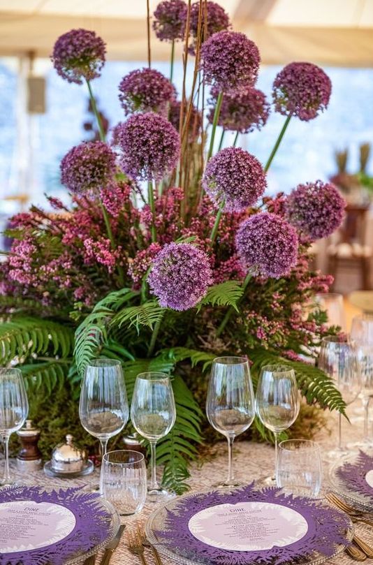 a bold and tall wedding centerpiece of pink blooms and fern and large alliums is a fantastic purple statement