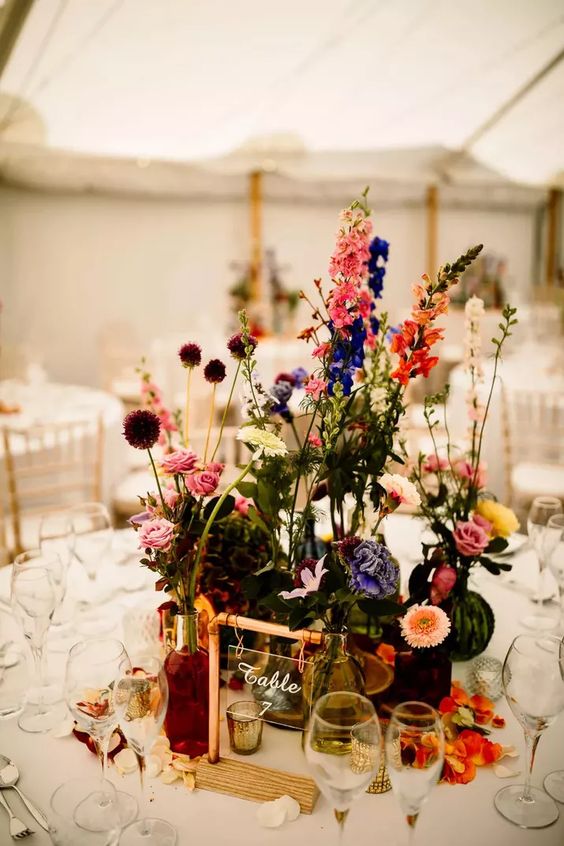 a bold wedding centerpiece of violet, pink, yellow, orange and blue blooms including roses, dahlias and allium is wow