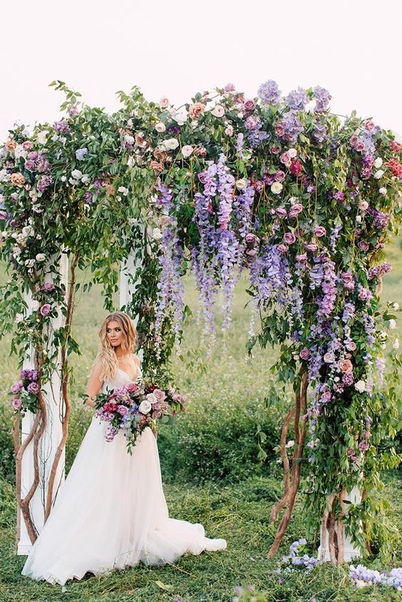 a cool summer wedding arch decorated with lots of white, lilac, mauve, peachy, pink and purple blooms including delphinium, and greenery