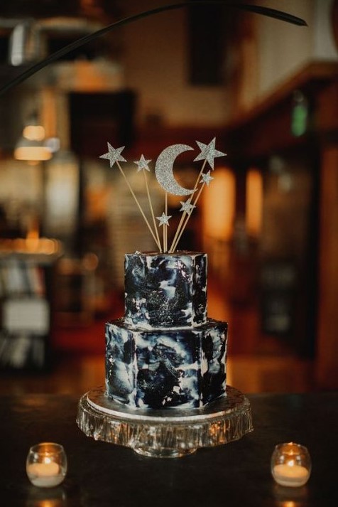 a dark watercolor wedding cake topped with silver glitter stars and moon on a shiny silver stand