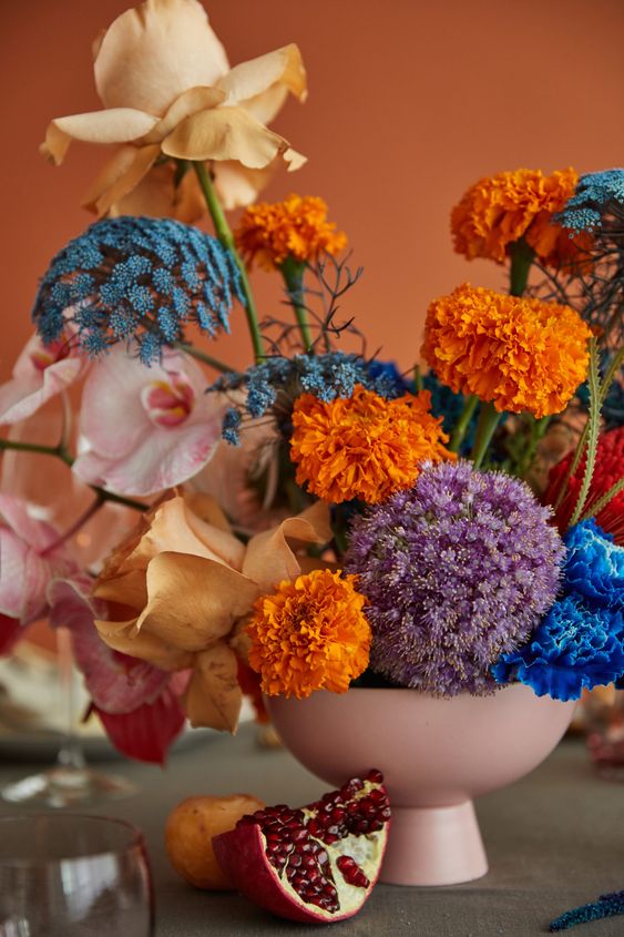 a colorful and dimensional wedding centerpiece of a blush bowl, yellow, orange, electric blue blooms including allium