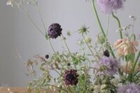 28 a refined and dimensional wedding centerpiece with lots of greenery, allium, deep purple blooms and thistles is beautiful