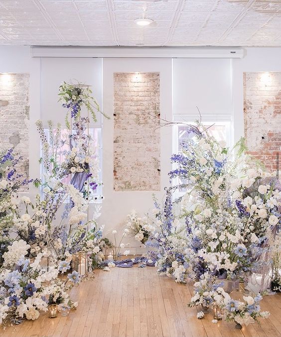 an indoor garden-inspired wedding altar made of white and purple delphinium, white blooms and greenery and candles on the floor