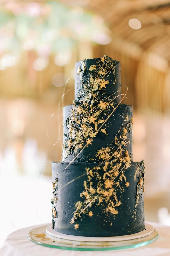 a midnight blue wedding cake decorated with gold leaf, with gold stars and sparkles, with a bit of gold swirls is wow