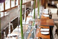 31 a very laconic modern wedding tablescape with an uncovered table, tall glass vases with allium is a chic and lovely idea