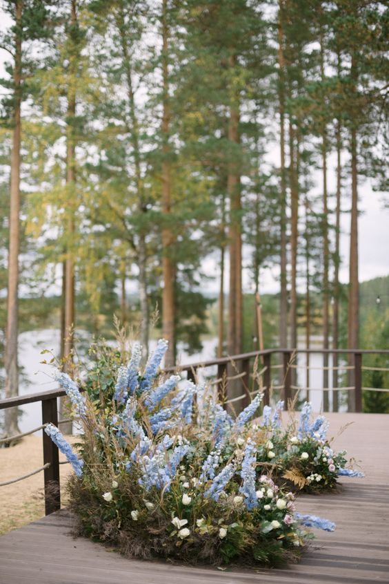 an outdoor wedding altar made of greenery, white blooms and blue delphinium is a gorgeous idea for a spring wedding