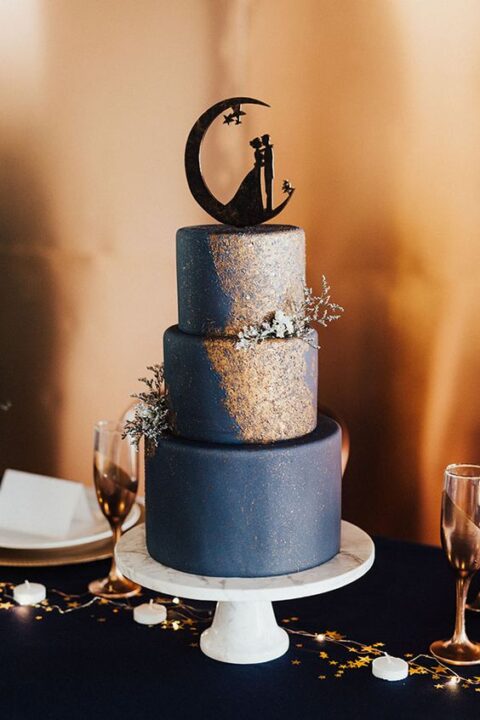 a navy and gold starry night wedding cake with a couple cake topper and some blooms is great for a romantic celestial wedding