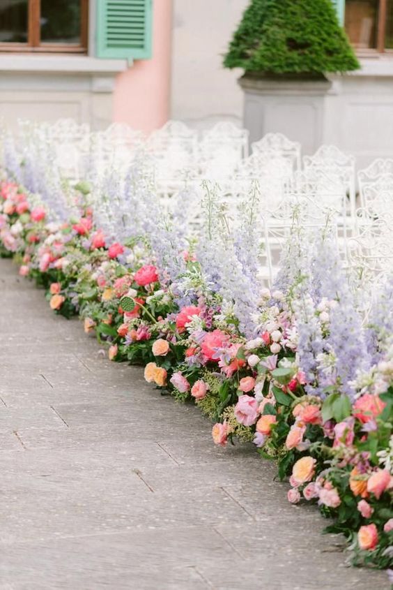 chic and colorful wedding summer aisle decor done with greenery, pink and orange peony roses and purple delphinium