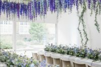 43 a wedding reception space accented with purple and blue blooms on the table and with purple, white and blue delphinium hanging down