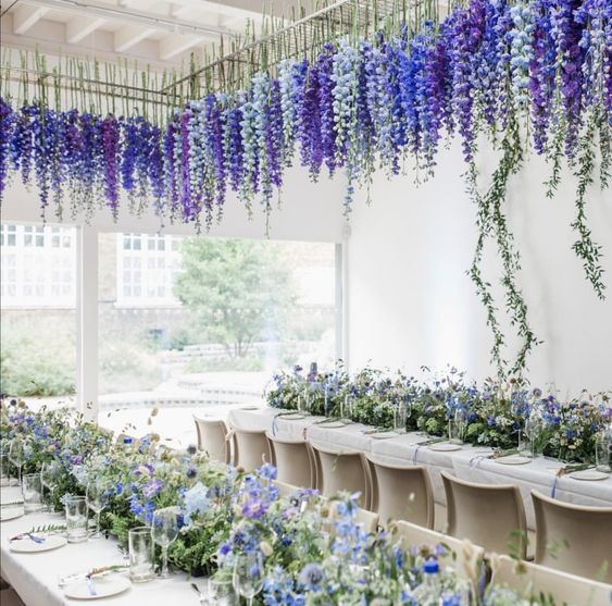a wedding reception space accented with purple and blue blooms on the table and with purple, white and blue delphinium hanging down
