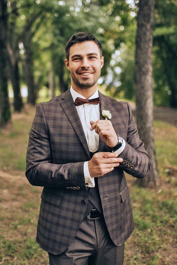 a brown plaid three piece pantsuit, a white shirt, a brown bow tie and a simple white flower boutonniere for a fall wedding