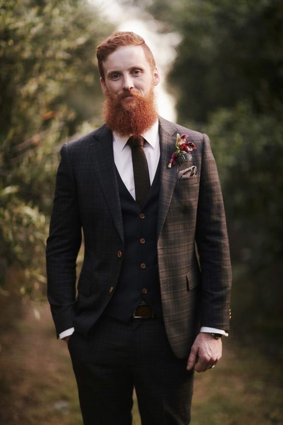 a brown plaid three piece suite with a brown tie and a white shirt, a taupe handkerchief and a bold floral boutonniere