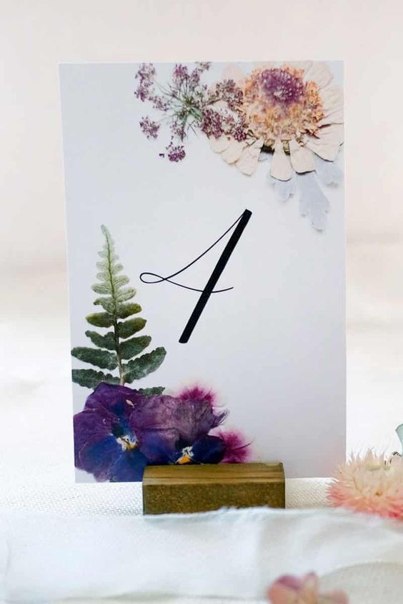 a super cool and bright pressed flower wedding table number with purple blooms and a leaf is amazing