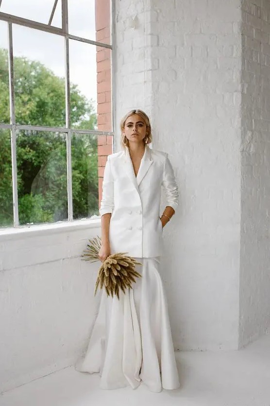 a chic and minimalist bridal look with an oversized white blazer and a maxi pleated skirt plus a grass wedding bouquet and statement earrings