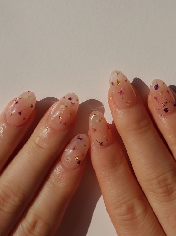 a delicate blush manicure with small dried flowers and gold leaf touches is perfect for both spring and summer
